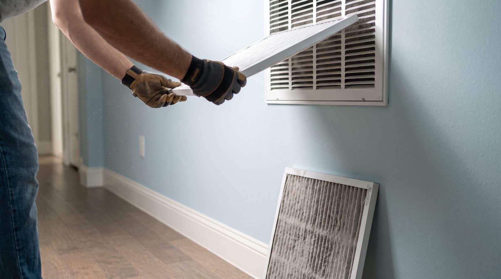 A new pleated air filter being slid into a hallway return grille